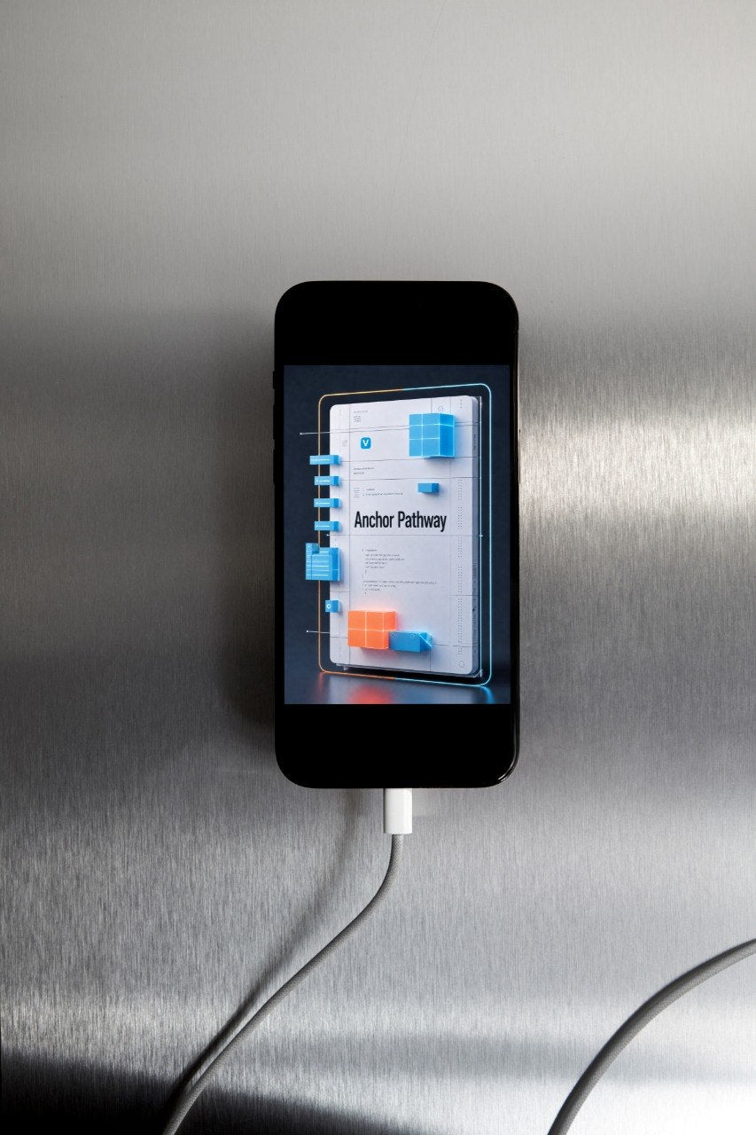 A black smartphone lies on a brushed metal surface with a white charging cable plugged into it. The phone screen displays a digital interface with the text 'Anchor Pathway' and blue and orange graphic blocks.
